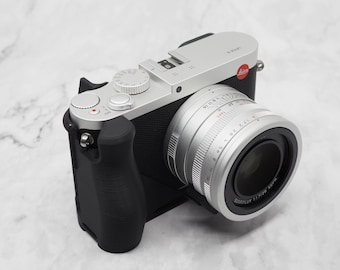 May include: A silver and black camera with a black grip and a silver lens. The camera has a red logo on the top.