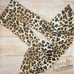 May include: A pair of brown and white leopard print bell bottom pants with a ruffled hem. The pants are made of a soft, stretchy fabric and are perfect for a casual, trendy look.  Peace Jove & Embroidery.