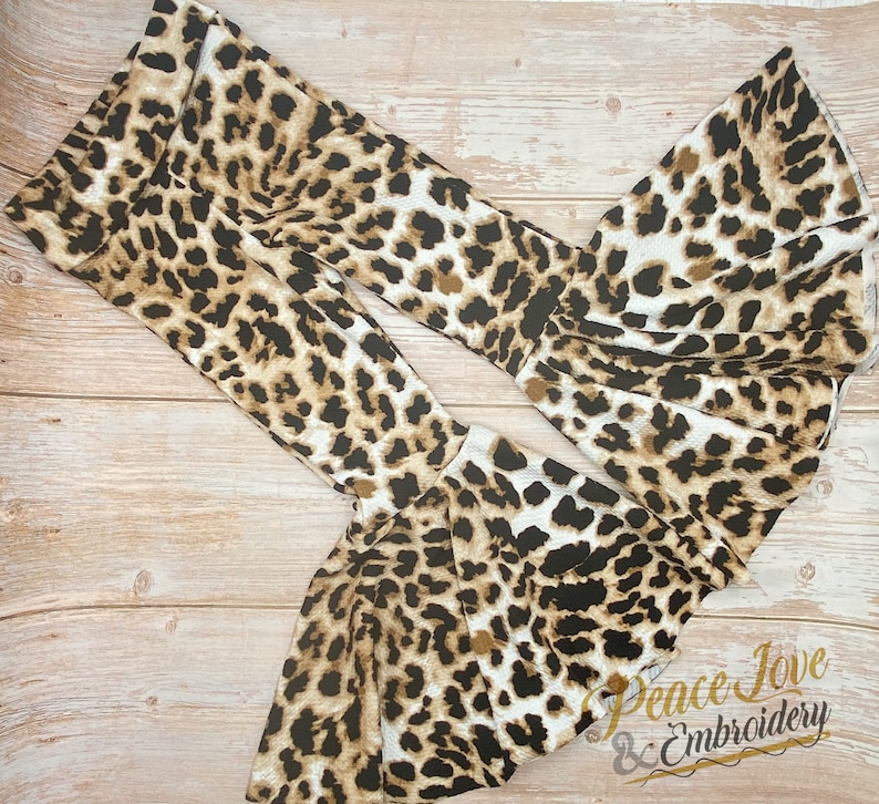 May include: A pair of brown and white leopard print bell bottom pants with a ruffled hem. The pants are made of a soft, stretchy fabric and are perfect for a casual, trendy look.  Peace Jove & Embroidery.