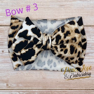 May include: A brown and black leopard print headband with a large bow. The headband is made of a soft, stretchy material and is perfect for adding a touch of style to any outfit.