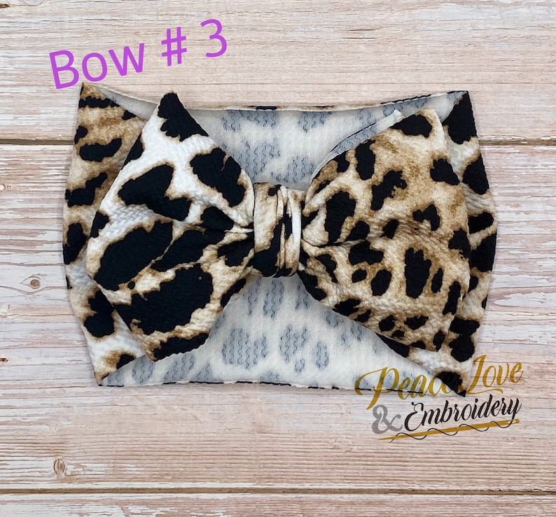 May include: A brown and black leopard print headband with a large bow. The headband is made of a soft, stretchy material and is perfect for adding a touch of style to any outfit.