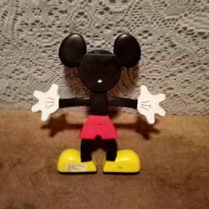 May include: A black and white plastic Mickey Mouse toy with red shorts and yellow shoes. The toy is articulated at the arms, legs, and head.