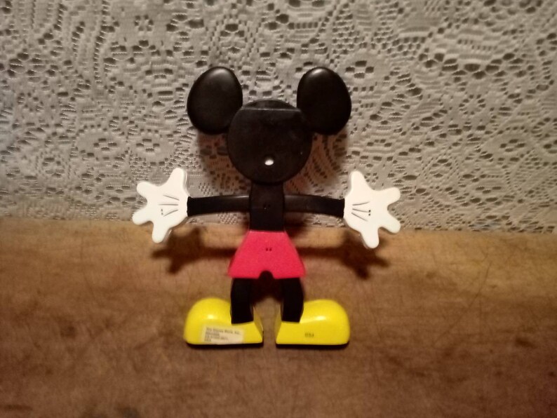 May include: A black and white plastic Mickey Mouse toy with red shorts and yellow shoes. The toy is articulated at the arms, legs, and head.