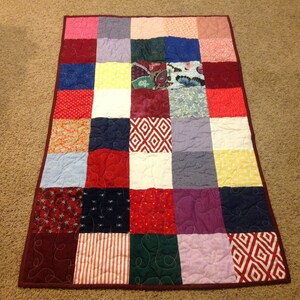 May include: A patchwork quilt with a variety of colors and patterns, including red, blue, green, yellow, and purple. The quilt is made up of squares of different fabrics, each with a unique design. The quilt is quilted with a simple pattern of swirls.