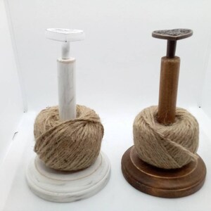 May include: Two wooden yarn holders with spools of twine. The holder on the left is painted white and has a heart-shaped top. The holder on the right is brown wood with a heart-shaped top.