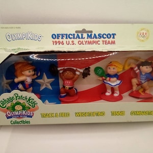 May include: A set of four Cabbage Patch Kids Olympikids figurines. The figurines are dressed in red, white, and blue outfits and are holding various sports equipment, including a track and field baton, a weightlifting barbell, a tennis racket, and a gymnastics ribbon. The figurines are standing on a red, white, and blue background with stars. The packaging includes the text "Official Mascot 1996 U.S. Olympic Team".