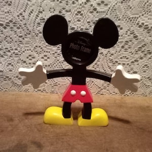 May include: Black plastic Mickey Mouse photo frame with a red and white polka dot shirt, white gloves, and yellow shoes. The frame says "Disney Photo Frame" on the front.