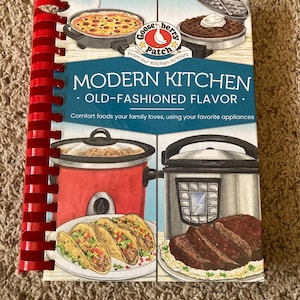 May include: A cookbook titled "Modern Kitchen - Old-Fashioned Flavor" with a red spiral binding. The cover features illustrations of various dishes and kitchen appliances. The Gooseberry Patch logo is visible.