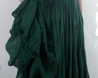 May include: A green, ruffled, sleeveless dress with a lace-up bodice and a black, ruffled, short-sleeved top underneath. The dress is worn by a mannequin with blonde hair and a black feathered hat.