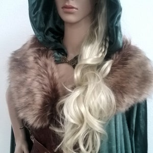 Puede incluir: Una mujer con una capa de terciopelo verde con capucha y cuello de piel marr&oacute;n. Lleva un cors&eacute; de cuero marr&oacute;n con una hebilla de metal. Su cabello rubio est&aacute; trenzado.