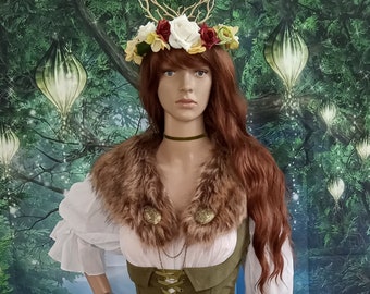 May include: A white long-sleeved dress with a layered skirt, paired with an olive green corset-style bodice featuring front lacing. The outfit includes a brown faux fur collar with two gold-toned circular brooches and a floral headpiece.