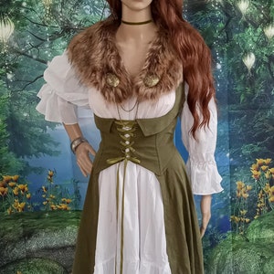 May include: A green and white dress with a brown fur collar and a green corset. The dress has a lace-up front and a white skirt with a ruffle at the bottom. The model is wearing a flower crown with antlers.