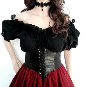May include: A black off-the-shoulder blouse with a lace-up corset belt and a red skirt. The blouse has ruffled sleeves and the corset has silver eyelets.