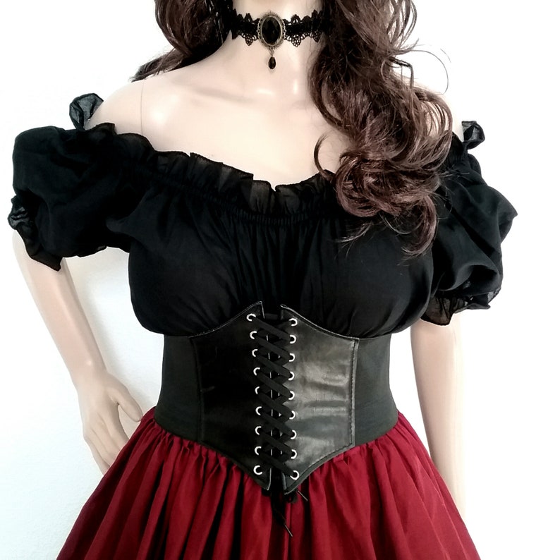 May include: A black off-the-shoulder blouse with a lace-up corset belt and a red skirt. The blouse has ruffled sleeves and the corset has silver eyelets.