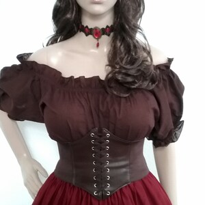 May include: A brown off-the-shoulder peasant top with a brown leather corset and a burgundy skirt. The model is wearing a white flower crown and a red jeweled choker.
