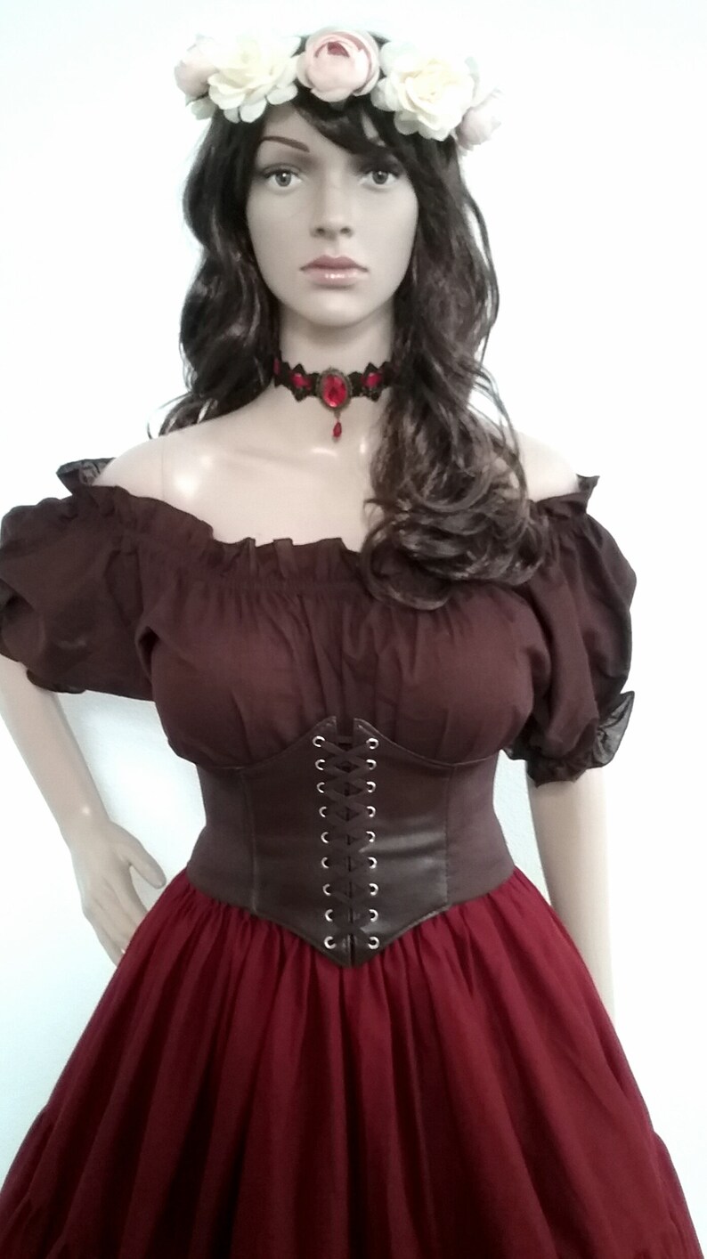 May include: A brown off-the-shoulder peasant top with a brown leather corset and a burgundy skirt. The model is wearing a white flower crown and a red jeweled choker.