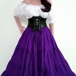 K&ouml;nnte beinhalten: Ein Outfit im Renaissance-Stil auf einer Schaufensterpuppe. Es besteht aus einer wei&szlig;en schulterfreien Bluse, einem schwarzen Korsett und einem langen, mehrschichtigen lila Rock. Ein Blumenkranz und ein Halsband vervollst&auml;ndigen das Ensemble. Der Rock ist bodenlang.