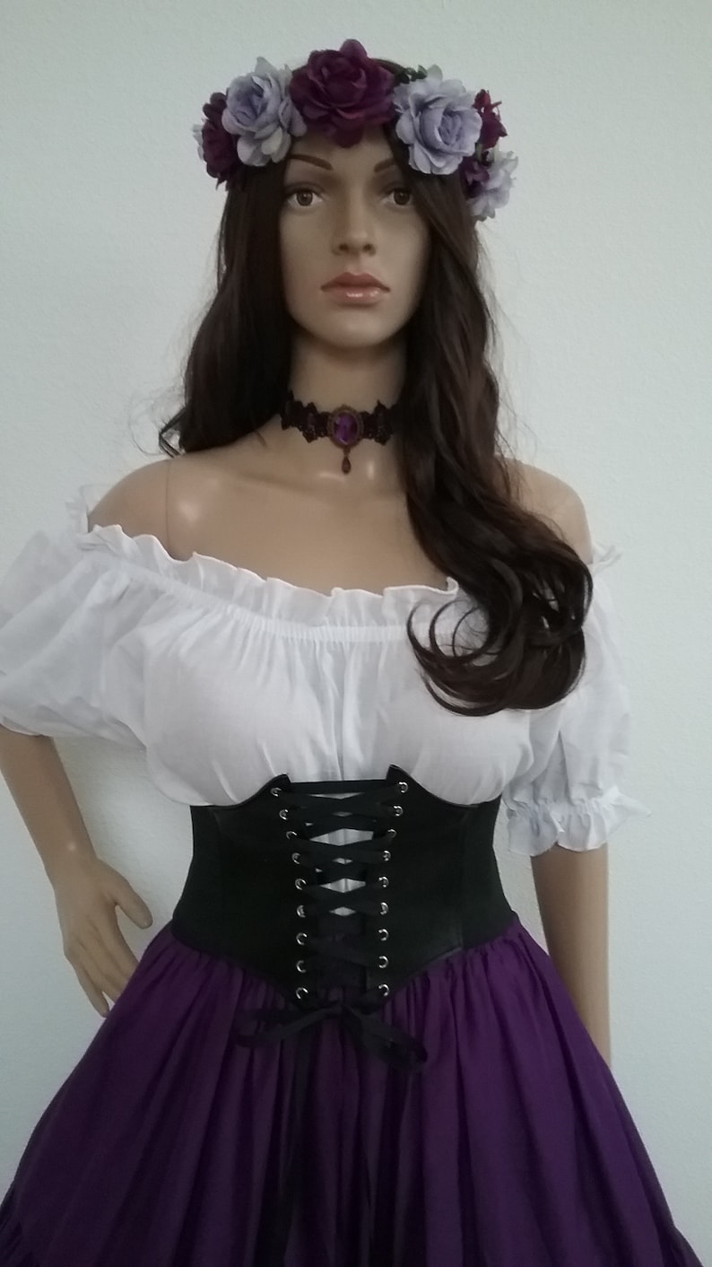 K&ouml;nnte beinhalten: Mannequin mit wei&szlig;er schulterfreier Bluse, schwarzem Korsett mit Schn&uuml;rdetails und langem lila Rock. Ein Blumenkranz mit lila und lavendelfarbenen Blumen schm&uuml;ckt den Kopf, und ein schwarzes Halsband mit lila Anh&auml;nger.