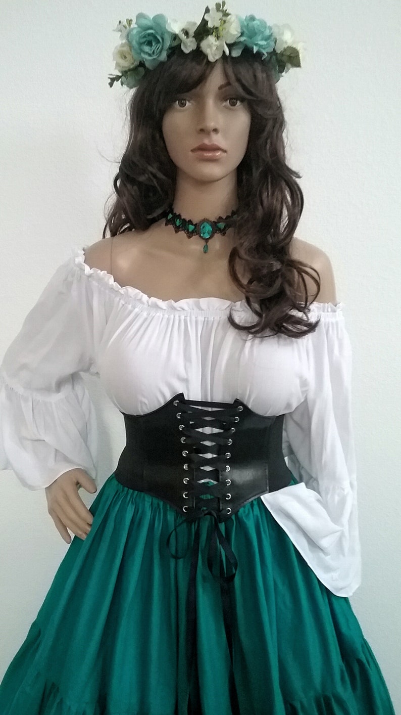 K&ouml;nnte beinhalten: Ein Outfit im Renaissance-Stil mit einer wei&szlig;en schulterfreien Bluse mit langen &Auml;rmeln, einem schwarzen Korsett und einem teal-gr&uuml;nen Rock. Das Ensemble wird durch einen Blumenkranz und einen passenden Choker erg&auml;nzt.