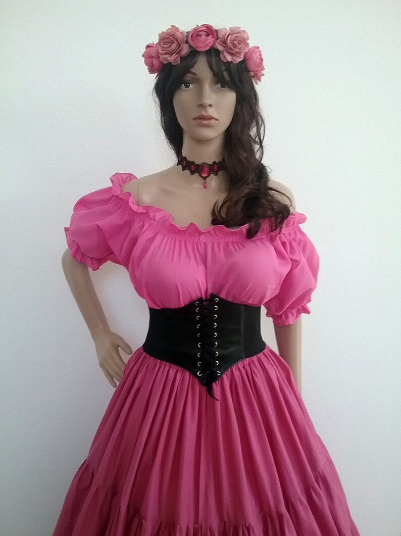 May include: A pink off-the-shoulder peasant top with a black corset belt and a pink flower crown. The top has a ruffled neckline and short sleeves.