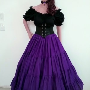 May include: A purple, tiered skirt with a black corset and a black off-the-shoulder top. The model is wearing a flower crown with purple and gray flowers.