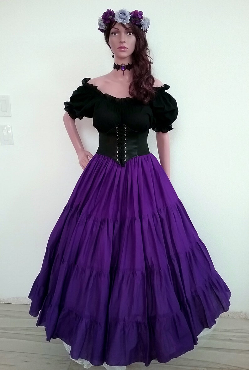 May include: A purple, tiered skirt with a black corset and a black off-the-shoulder top. The model is wearing a flower crown with purple and gray flowers.