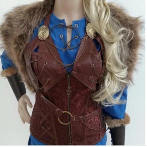 May include: A brown leather corset with a chain detail and a fur collar. The corset has a zipper closure and a belt with a metal buckle. The corset is worn over a blue shirt.