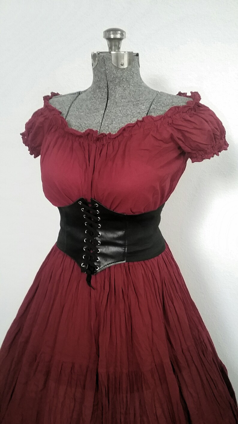 May include: A maroon off-the-shoulder dress with a black leather corset belt. The dress has a ruffled neckline and a tiered skirt.
