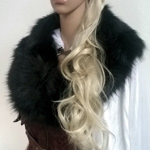 Puede incluir: Una peluca rubia con trenzas peinada con una diadema de cuero marr&oacute;n. La peluca la lleva un maniqu&iacute; con un cuello de piel sint&eacute;tica negra y un cors&eacute; de cuero marr&oacute;n. El maniqu&iacute; lleva una bata blanca.
