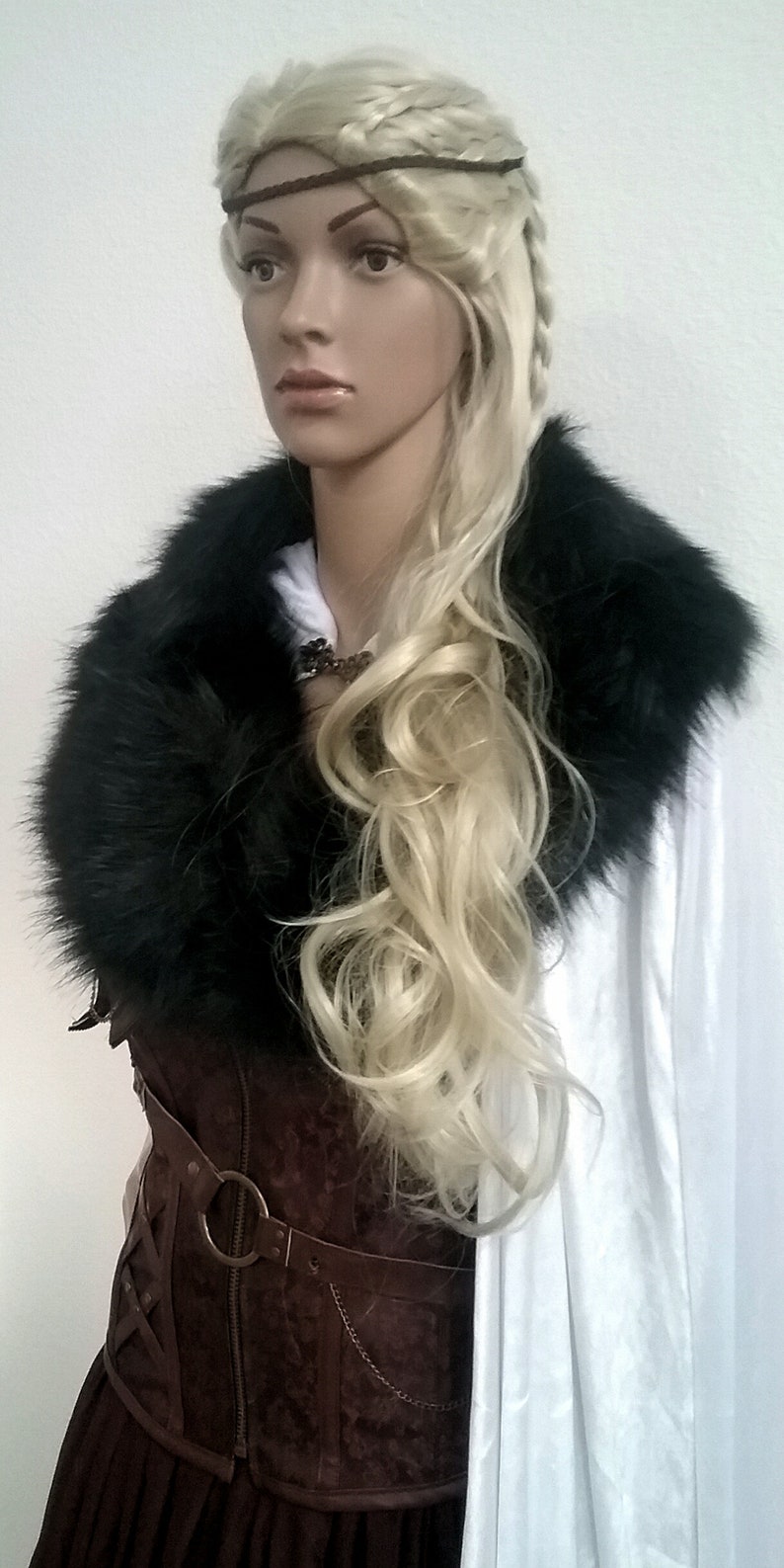 Puede incluir: Una peluca rubia con trenzas peinada con una diadema de cuero marr&oacute;n. La peluca la lleva un maniqu&iacute; con un cuello de piel sint&eacute;tica negra y un cors&eacute; de cuero marr&oacute;n. El maniqu&iacute; lleva una bata blanca.