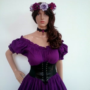 May include: A purple off-the-shoulder peasant top with a black leather corset and a flower crown. The crown is made of purple and white flowers.