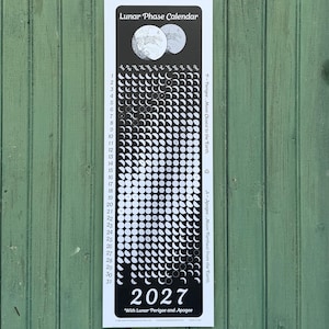 May include: A vertical 2027 Lunar Phase Calendar printed on a black background with white text and moon phase illustrations. The calendar displays months from January to December, days 1 through 31, and notes for Lunar Perigee and Apogee.