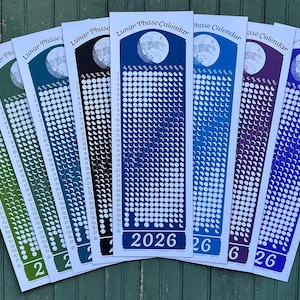 May include: A collection of colorful lunar phase calendars for the year 2026. Each calendar features a different color scheme, with a moon graphic at the top and a series of white circles and crescent shapes representing the moon's phases.