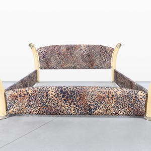 May include: A bed frame with a leopard print fabric headboard and side rails. The frame has light-colored, curved legs with decorative brass-colored accents. The bed frame is designed for a standard mattress.