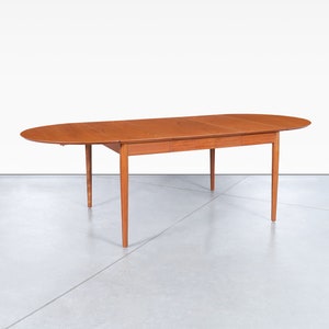 May include: A mid-century modern oval dining table with a wood top and four legs. The table has a leaf that extends the length of the table.