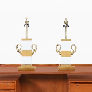 May include: Two matching table lamps with a mid-century modern design. Each lamp features a white and wood-toned rectangular body with gold-colored accents and a brass-colored neck. The lamps are placed on a wooden desk.