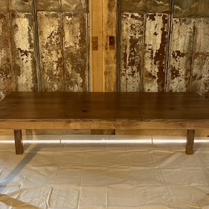 Puede incluir: Una mesa de comedor de madera maciza con una tapa de madera marrón y cuatro patas. La mesa está sobre una superficie blanca.