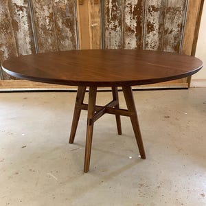 May include: A round wooden table with a dark brown finish and a simple, modern design. The table has a circular top and a four-legged base with a cross-shaped support.