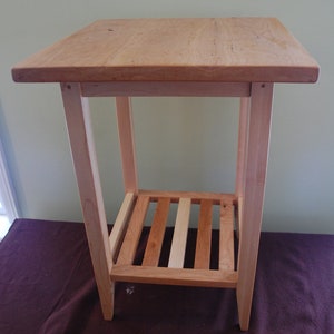 May include: A wooden end table with a single shelf. The table is made of light wood and has a simple, rectangular design.