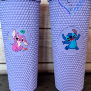 Puede incluir: Dos vasos morados con tachuelas y pajitas a juego. Un vaso presenta un personaje de dibujos animados rosa, el otro un personaje de dibujos animados azul. Los vasos tienen una pegatina redonda con la imagen del personaje.