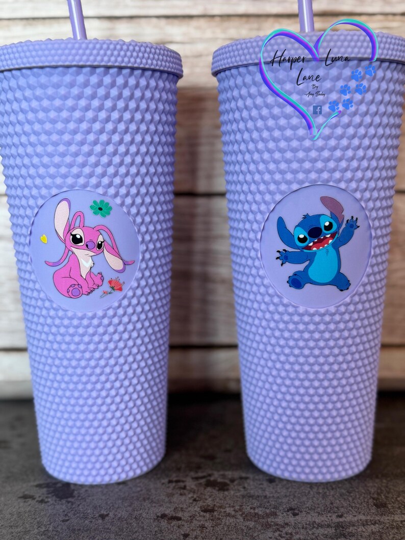 Puede incluir: Dos vasos morados con tachuelas y pajitas a juego. Un vaso presenta un personaje de dibujos animados rosa, el otro un personaje de dibujos animados azul. Los vasos tienen una pegatina redonda con la imagen del personaje.