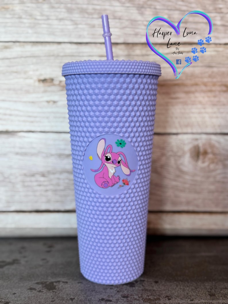 Puede incluir: Un vaso de color lavanda con tachuelas, con tapa y pajita a juego. Una calcoman&iacute;a circular presenta un personaje de dibujos animados rosa con orejas grandes y una flor. El vaso est&aacute; dise&ntilde;ado con una superficie texturizada.