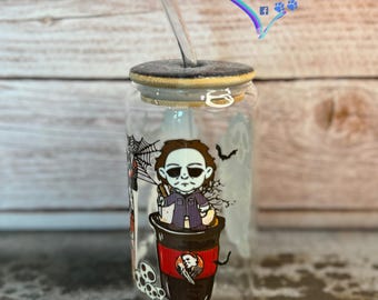May include: A clear glass tumbler with a black lid and a straw. The tumbler has a Halloween-themed design featuring a cartoon character from the movie Halloween. The design includes a spider web, a bat, and a coffee cup with the character sitting on top. The text "Harper Luna Lane" is visible on the image.