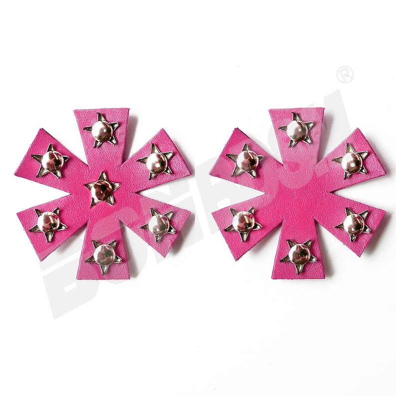 Puede incluir: Dos parches de estrella rosa con tachuelas plateadas. Cada parche tiene ocho puntas y una estrella plateada en el centro.