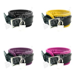 May include: Four leather collars with a lock and key. The collars are black with a contrasting colored trim. The colors are black, yellow, purple, and pink.