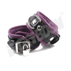May include: A pair of black leather cuffs with purple lining and a silver lock. The cuffs are designed for wrists and have a metal ring on one side.