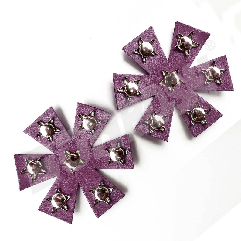 Puede incluir: Dos parches de cuero morado en forma de estrella con tachuelas plateadas. Cada parche tiene ocho puntas y una estrella plateada en el centro de cada punta.