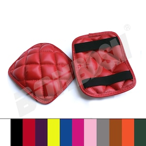 May include: Two red quilted leather motorcycle seat pads with black elastic straps. The pads are diamond-stitched and have a soft, plush texture.