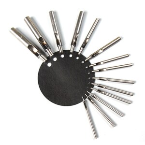 May include: A set of 12 silver leather hole punches of varying sizes, arranged in a circle on a black leather backing.