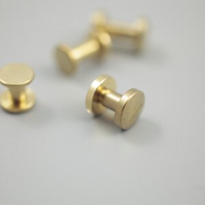 Op de afbeelding: Vier gouden metalen schroefknoppen met een ronde kop en een cilindrische basis.